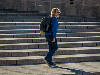 Side view of backpack woman walking on steps during sunny day