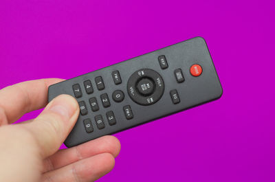 Cropped hand holding remote control against blue background