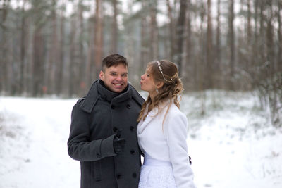 Portrait of groom with bride standing at forest during winter