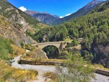 Arch bridge over river amidst mountains against sky