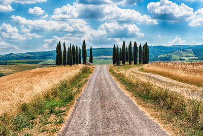 Empty road amidst field against sky