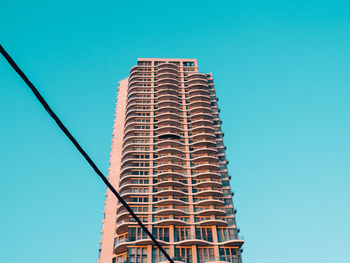 Low angle view of building and cable against clear blue sky in city