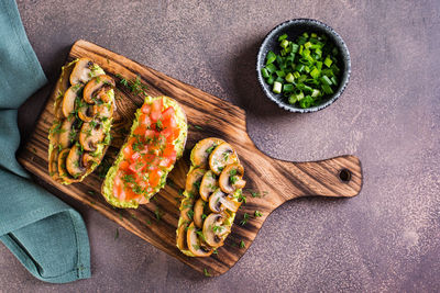 Sandwiches with avocado, fried champignons, tomatoes and herbs on rye bread on a board top view