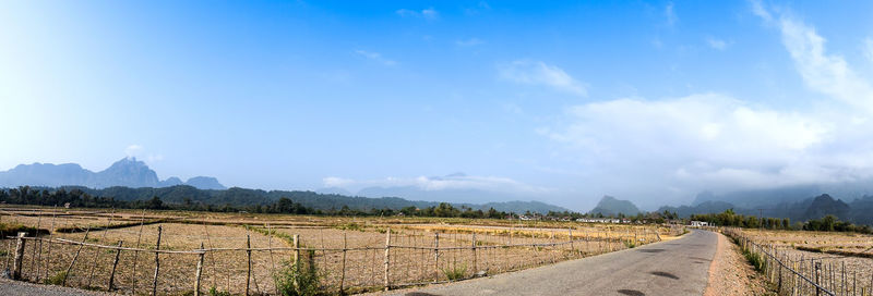 Panoramic view of road leading towards mountains against blue sky