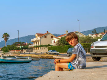 Rear view of young woman sitting at beach against clear sky
