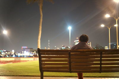 Rear view of man sitting on bench at night