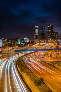 High angle view of light trails on road amidst buildings against sky at night