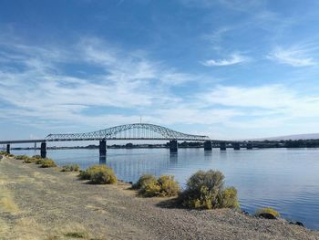 Suspension bridge over river against cloudy sky