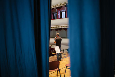 Rear view of man standing on stage seen through curtain