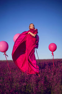 Beautiful young woman on a pink stepladder in a pink dress in a field with wildflowers in summer