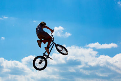 Silhouette of man jumping on bicycle against blue sky with white clouds. guy performs tricks on bike