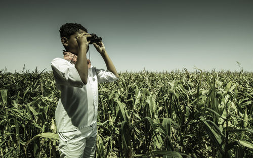 Boy looking through binoculars while standing on field