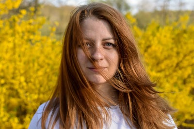 Portrait of young woman standing amidst yellow flowering plants on field