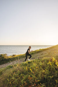 Side view of determined woman running on hill against sky