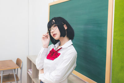 Young woman looking away while standing against wall