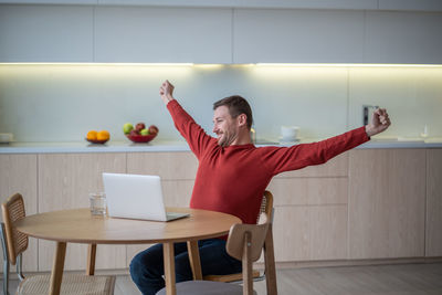 Smiling pleased happy man freelancer stretching arms in satisfaction, accomplishment of work ending