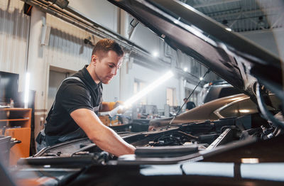 Under the hood. man in uniform is working in the auto service.