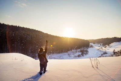 Rear view of woman gesturing on snow covered field against sky