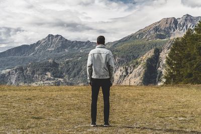 Rear view of man looking at mountains while standing on field