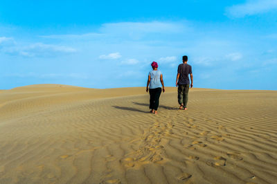 Rear view of people walking on sand dune