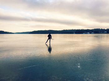 Rear view of person skating on frozen lake against sky
