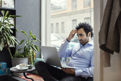 Worried businessman using laptop while sitting by window in office