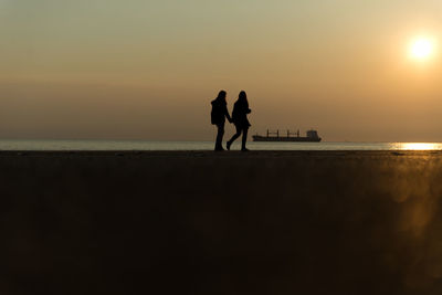 Silhouette men standing on beach against sky during sunset