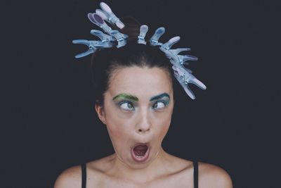 Young woman with clothespins on hair making funny face against black background