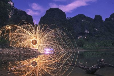 Illuminated trees by lake against sky at night