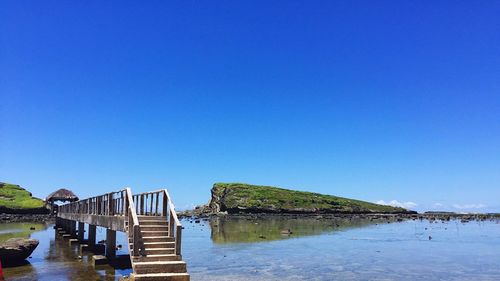 Pier over sea against clear blue sky