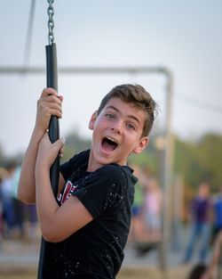 Portrait of smiling boy playing on swing against clear sky