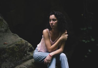 Young woman looking away while sitting on rock