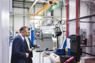 Two businessmen in factory shop floor examining machine