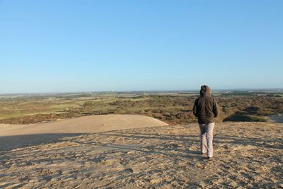 Rear view of woman standing on desert against clear sky