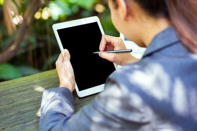 Midsection of woman using digital tablet on table while sitting outdoors