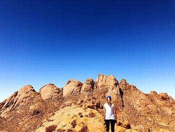 Rear view of woman standing on rock against sky