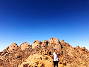 Rear view of woman standing on rock against clear blue sky