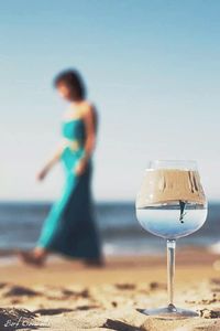 Woman standing by glass on beach against clear sky