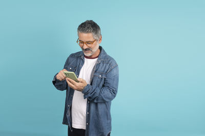 Young man using mobile phone while standing against blue background