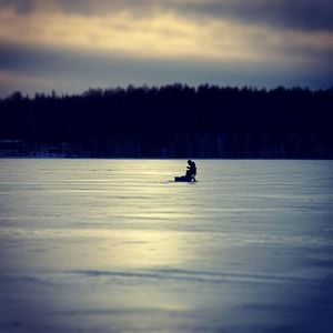 Silhouette person in frozen lake against sky during sunset