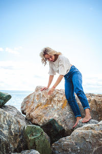 Young woman standing on rock at sea shore against sky