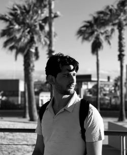 Young man looking away while standing on palm tree