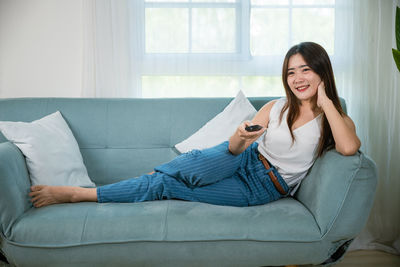 Young woman using phone while sitting on sofa at home