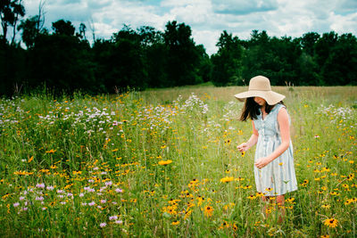 Rear view of woman standing on field by flowering plants