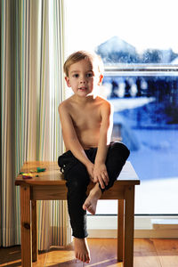 Portrait of shirtless boy sitting on table at home