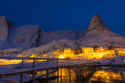 Illuminated buildings by mountains against clear blue sky at night norway