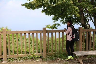 Full length of woman standing by railing against trees