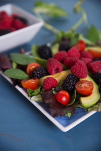 Salad with red berries, cherry tomatoes and avocado, on a blue table.