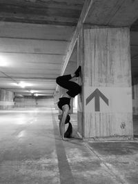 Side view of woman practicing handstand by column at illuminated parking garage