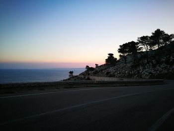 Road by sea against clear sky during sunset